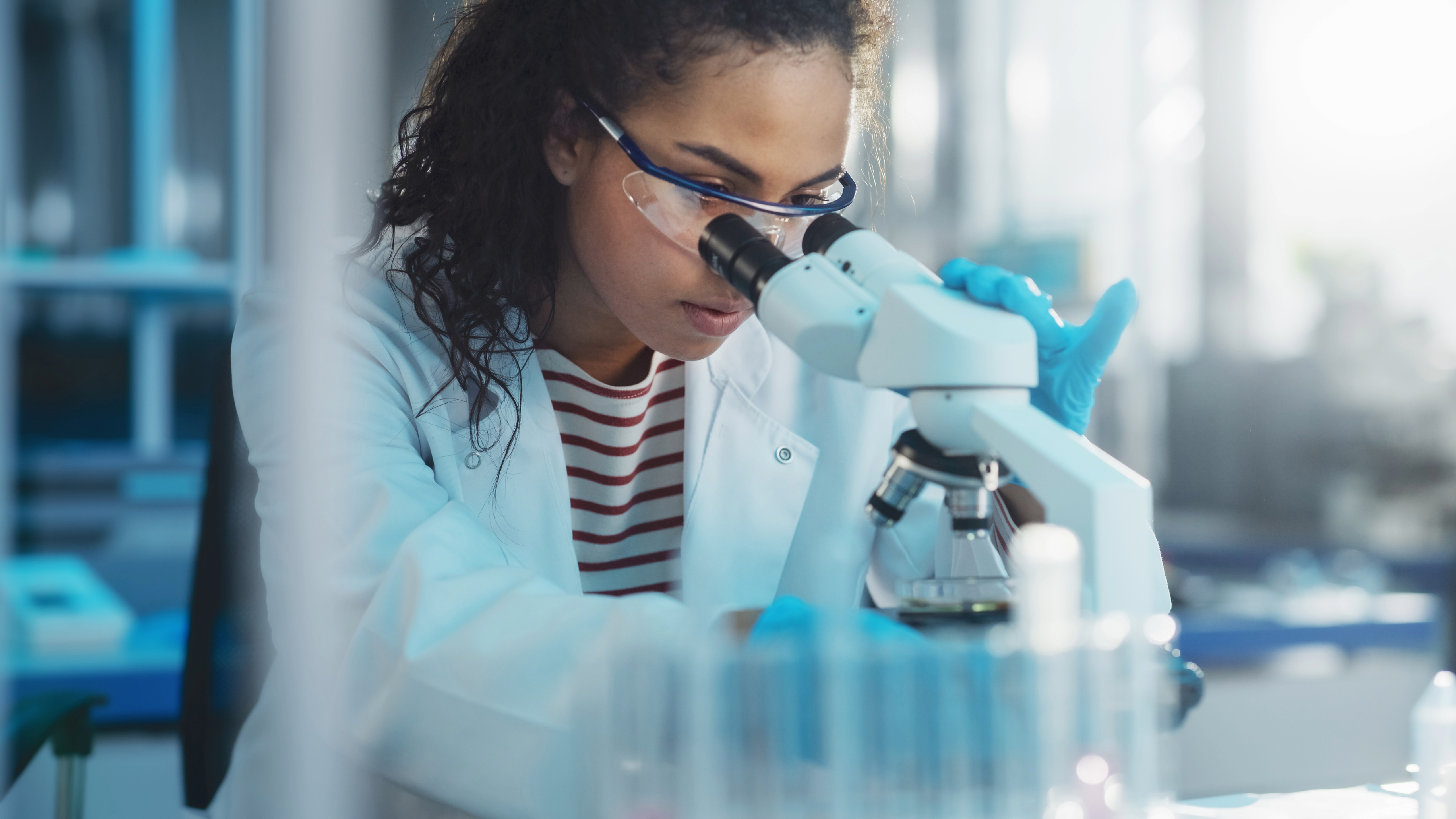 Student in lab coat peering into microscope