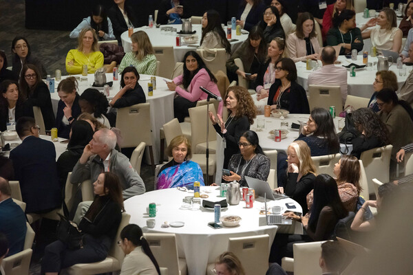 A questioner stands in front of microphone in a sea of seated attendees 