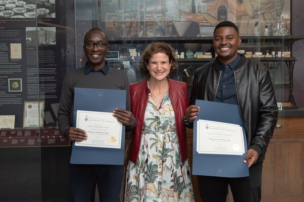 Med students holding certificates, on either side of doctor