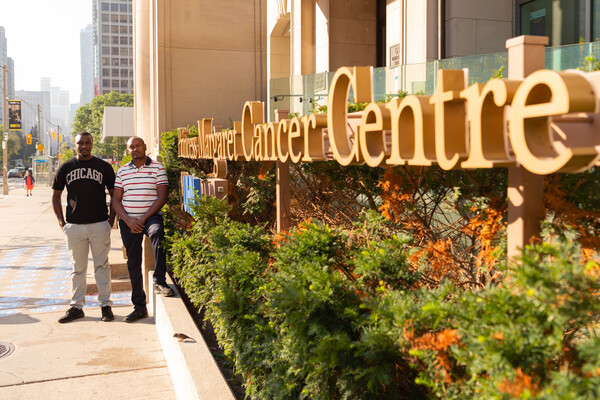 Two fellows in perspective beside Cancer Centre sign