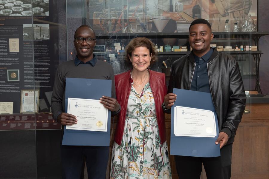 Med students holding certificates, on either side of doctor