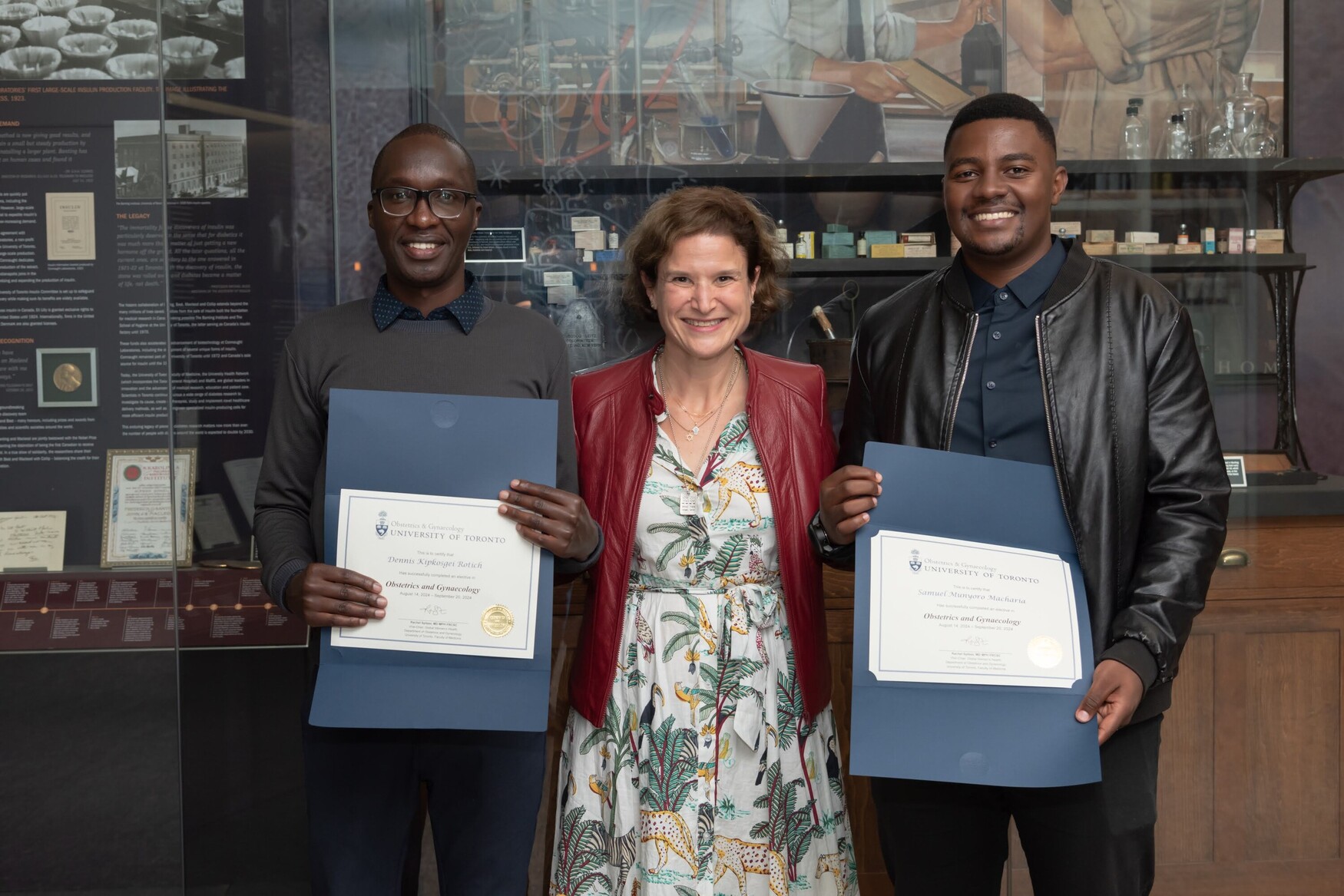 Med students holding certificates, on either side of doctor